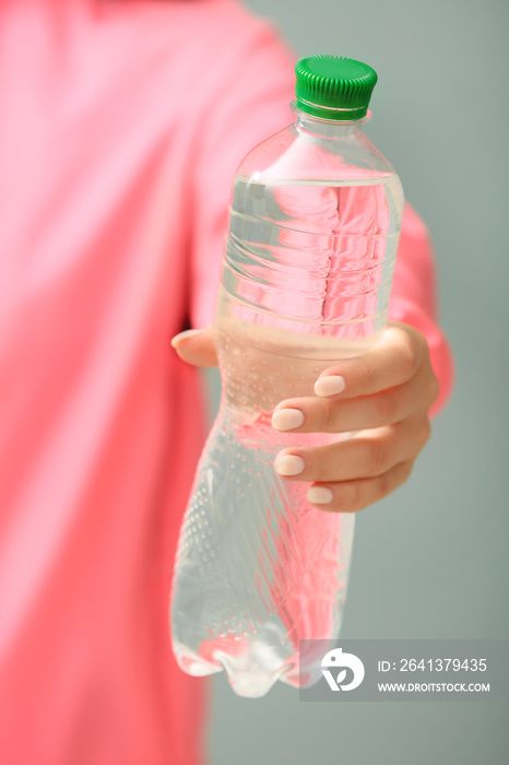 Sportswoman with bottle of fresh water on color background, closeup