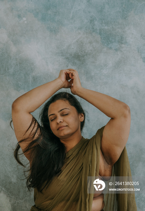 East Indian woman clasping hands overhead eyes closed