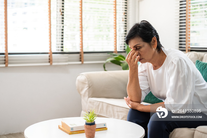 Senior old Asian woman feel stressed, headache sitting alone on sofa at home