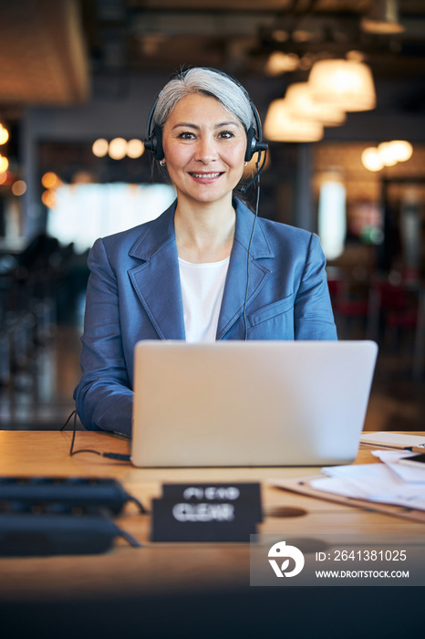 Cheerful woman in headphones using laptop at work