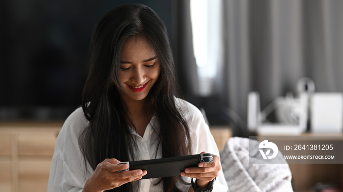 快乐的年轻女人穿着睡衣坐在沙发上，在客厅里玩电子游戏。