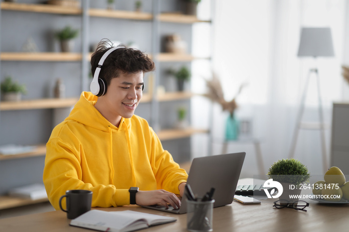 Smiling asian man in headset using laptop at home