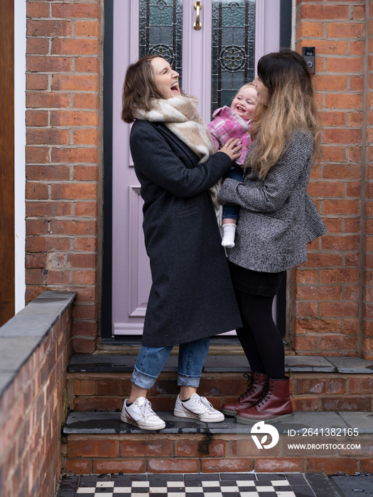 Women laughing and holding child in front of house�