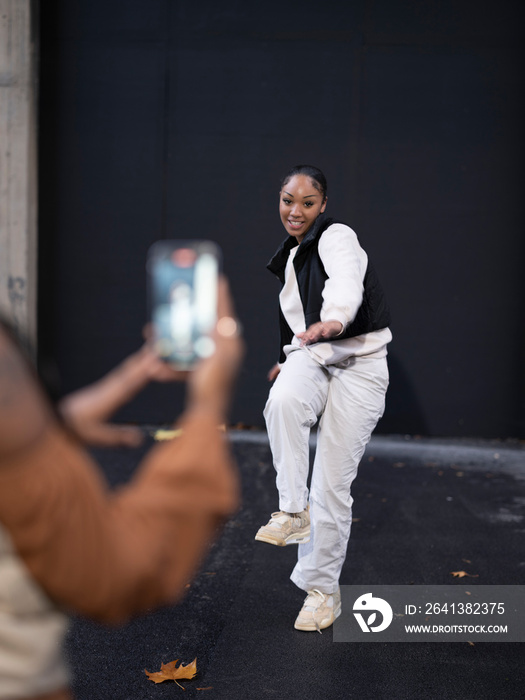 Young woman photographing?friend dancing in city