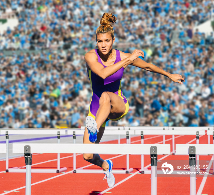 Runner jumping over hurdle on track