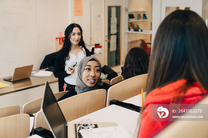 Smiling female friends sharing ideas in classroom at university