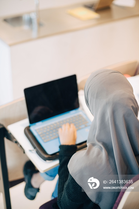 High angle view of female student using laptop at desk in classroom