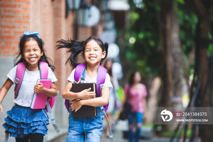 Back to school. Two cute asian child girls with school bag holding book and walk together in the sch