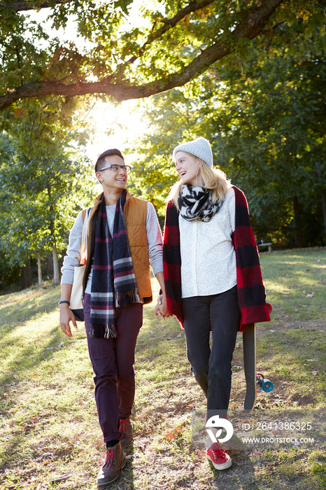 Young woman skateboarder holding hands and strolling with boyfriend in park