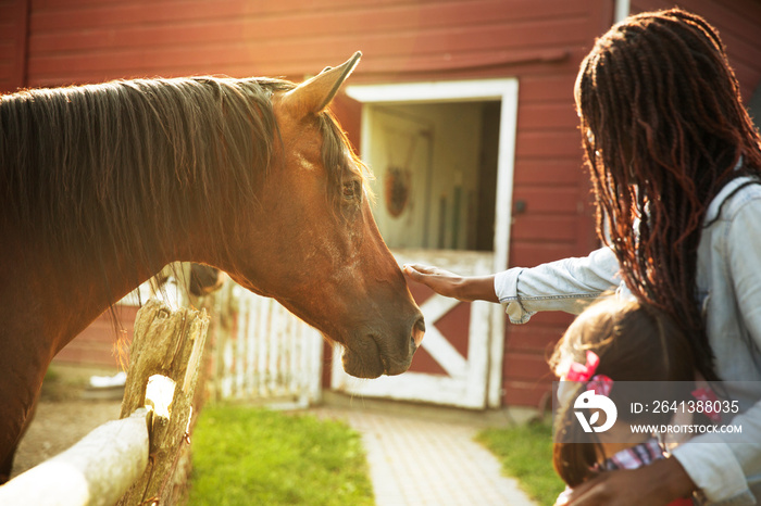 Woman and girl stroking horse on ranch