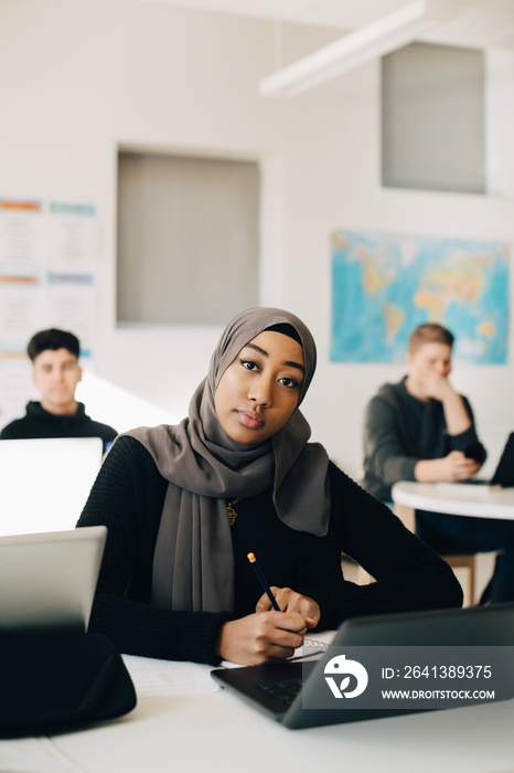 Portrait of female student wearing hijab is using laptop in classroom at university