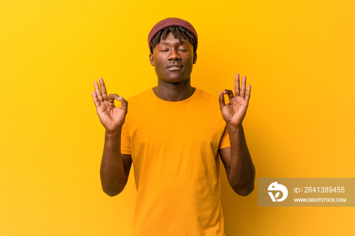 Young black man wearing rastas over yellow background relaxes after hard working day, he is performi