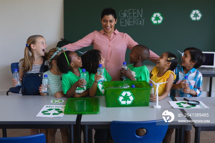 Happy schoolkids looking at teacher on desk in classroom