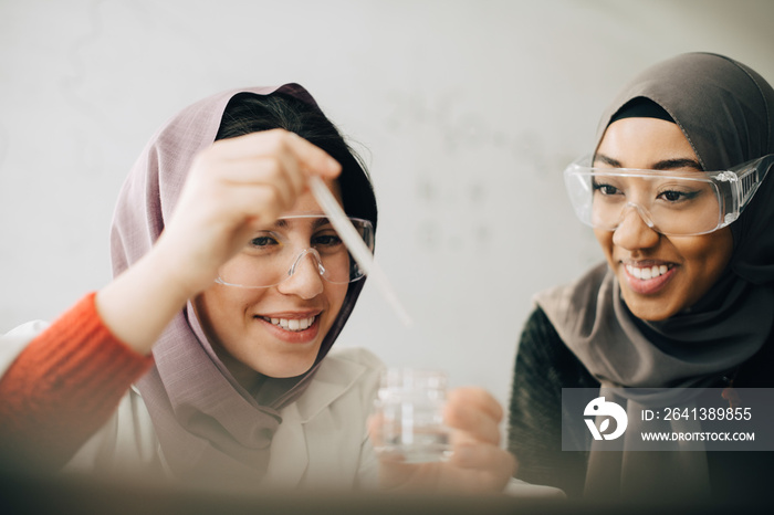 Smiling female students learning chemistry together in high school laboratory