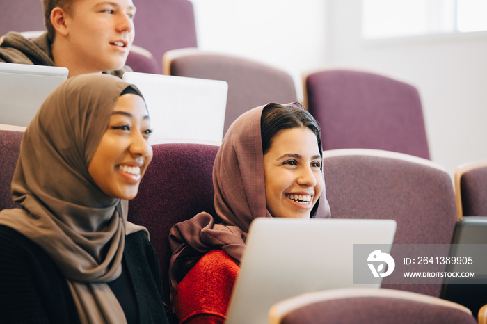 Smiling teenage classmates listening lectures in classroom at university