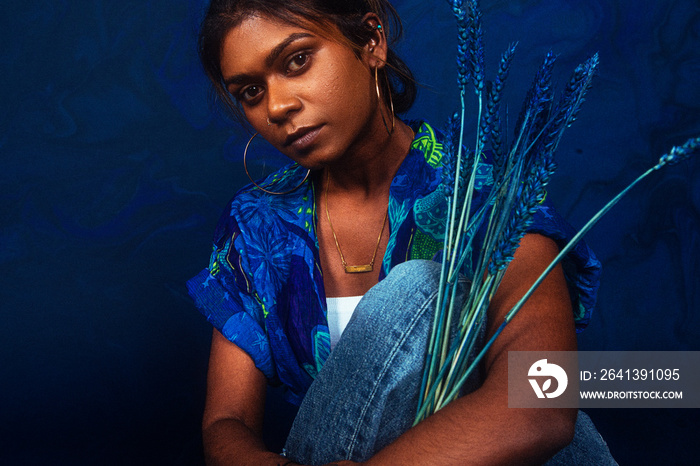 portrait of dark skinned Indian woman from Malaysia against a dark blue background with blue flowers