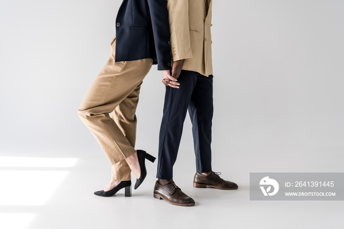 cropped shot of stylish young multiethnic couple standing back to back and holding hands on grey