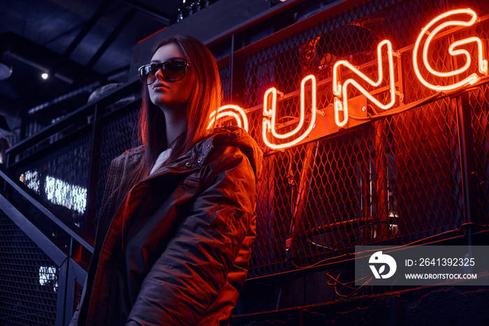 Young stylish girl wearing a hoodie coat and sunglasses standing on stairs at underground nightclub 