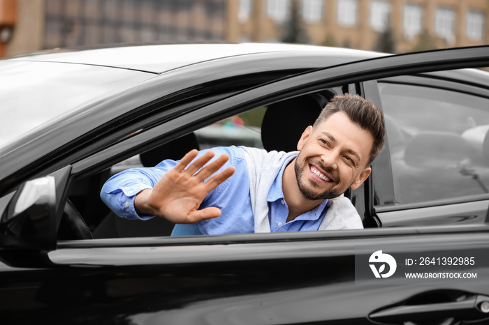 Handsome businessman waving hand in modern car