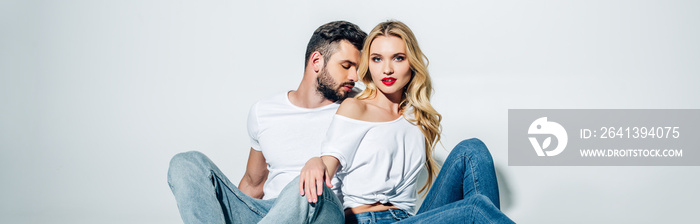 panoramic shot of handsome bearded man sitting and looking at attractive blonde girl on white