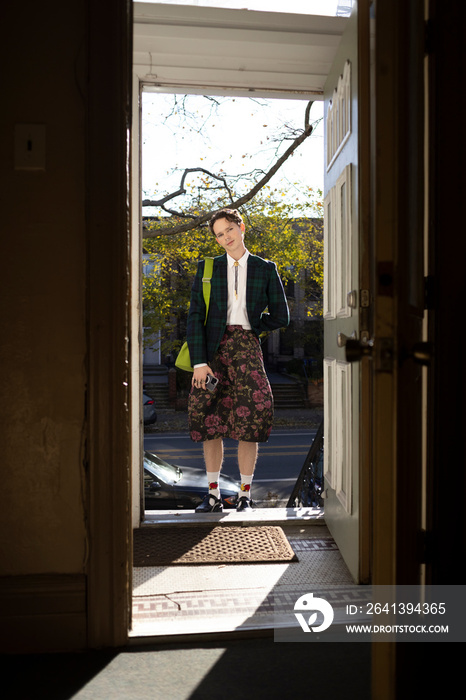 fashionable non-binary person wearing jacket and skirt in doorway