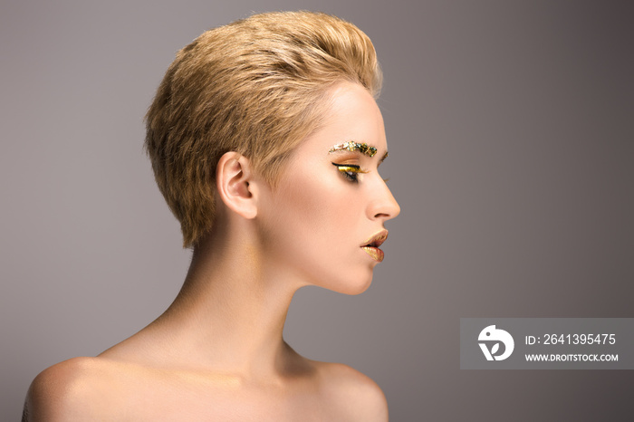 side view of attractive woman with golden shiny glitter on face isolated on grey