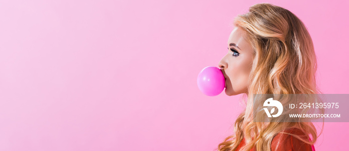 panoramic shot of beautiful girl blowing bubble gum isolated on pink, doll concept