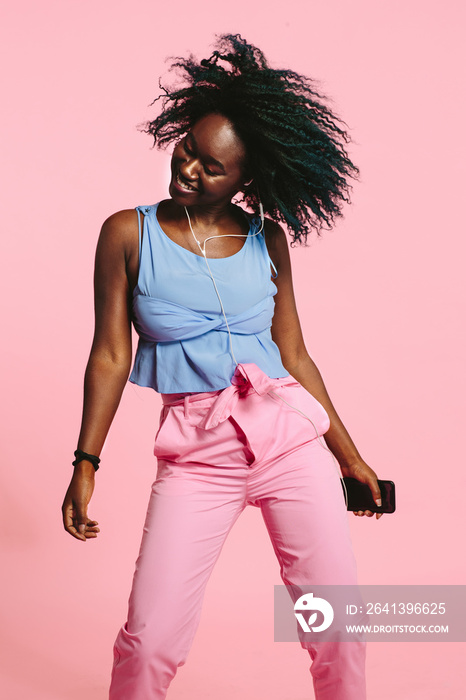 Smiling woman enjoying listening and dancing to music on her phone