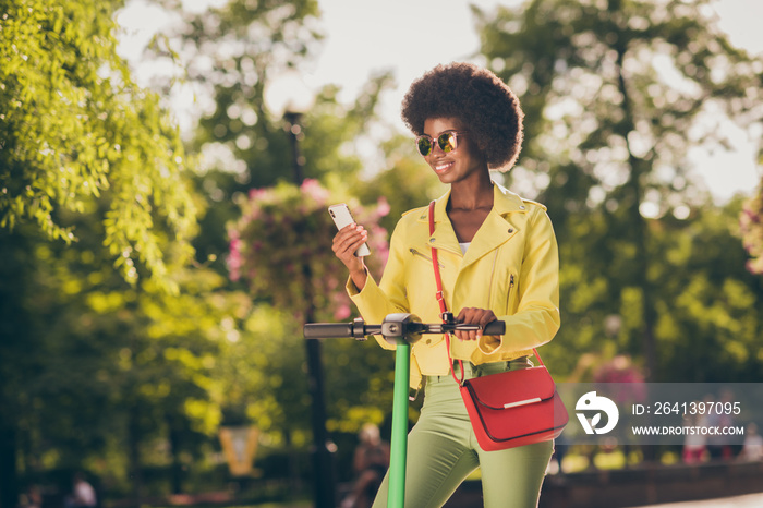 Photo portrait of woman riding green e-scooter holding phone in one hand wearing sunglasses outdoors