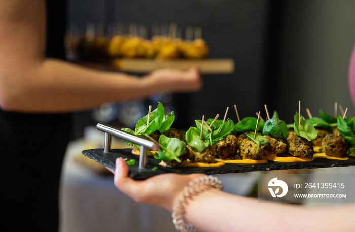 Serveuse avec un plateau dans les mains rempli de petites bouchées en forme de boules avec feuille d