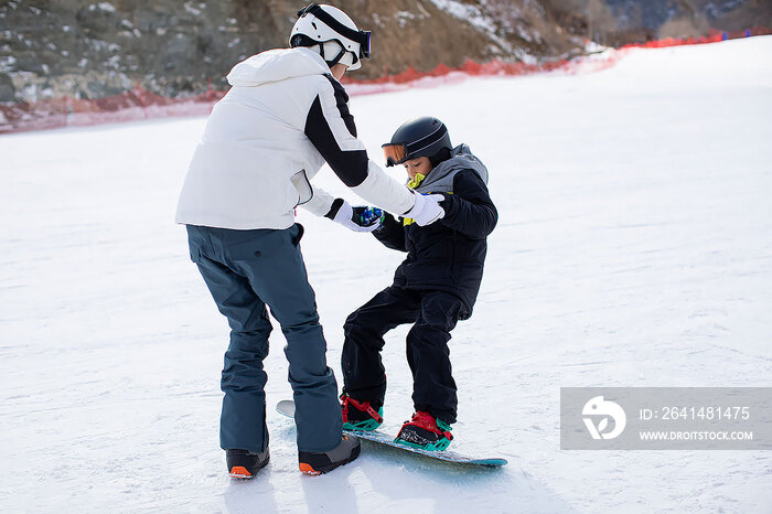 小男孩跟着教练在户外学滑雪