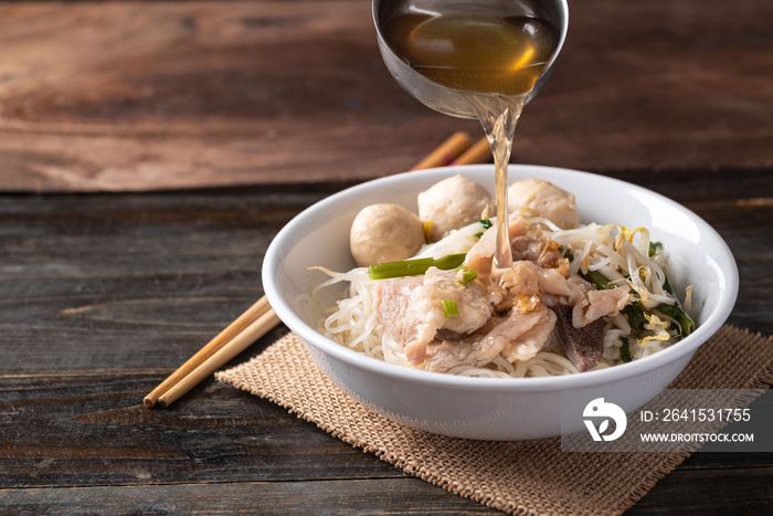 Rice noodles soup with pork and pork ball in a bowl with ladle pouring soup water, Thai noodles soup