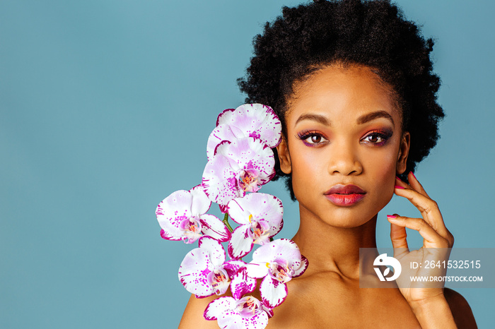 Portrait of a beautiful young woman with pink make up, lips, and orchid flower blooms around face