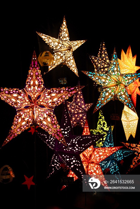 Brightly lit star lanterns with a black background. Photo taken at a German Christmas Market kiosk. 