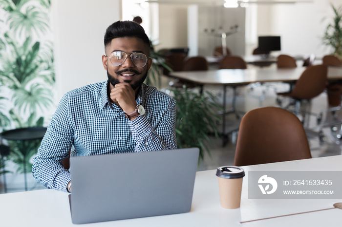 Young indian man smiling and working at modern office