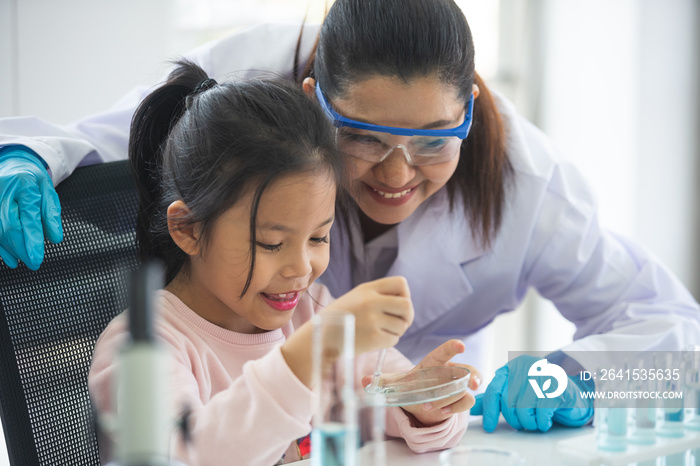 little asian children girl in elementary science class doing chemical experiment helped by woman tea