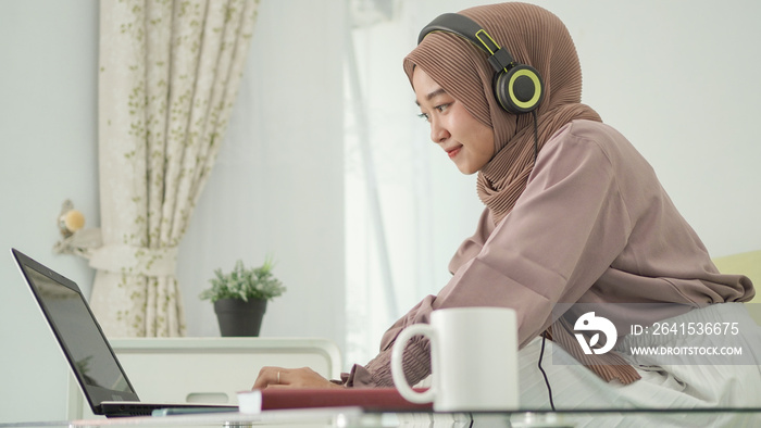 asian woman in hijab working from home happily listening