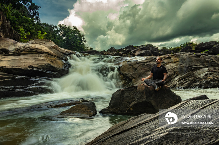 man meditating at rock with the beautiful waterfall stream at evening