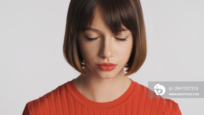 Portrait of attractive girl with bob hair and red lips dreamily closing eyes over white background