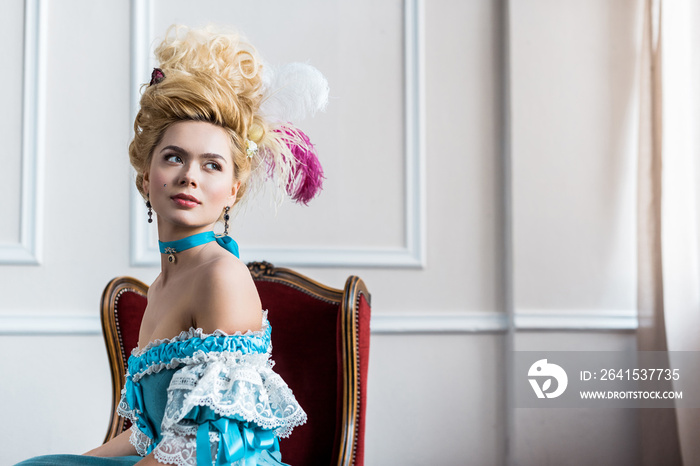 beautiful victorian woman in wig with feathers sitting on antique chair