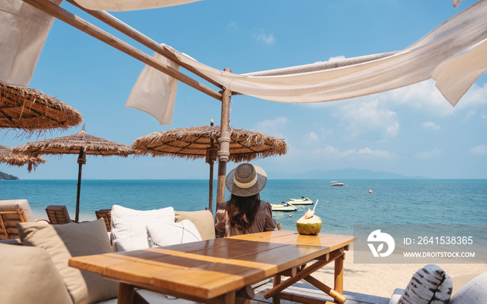 Rear view image of a woman looking at a beautiful sea while sitting in the cafe on the beach