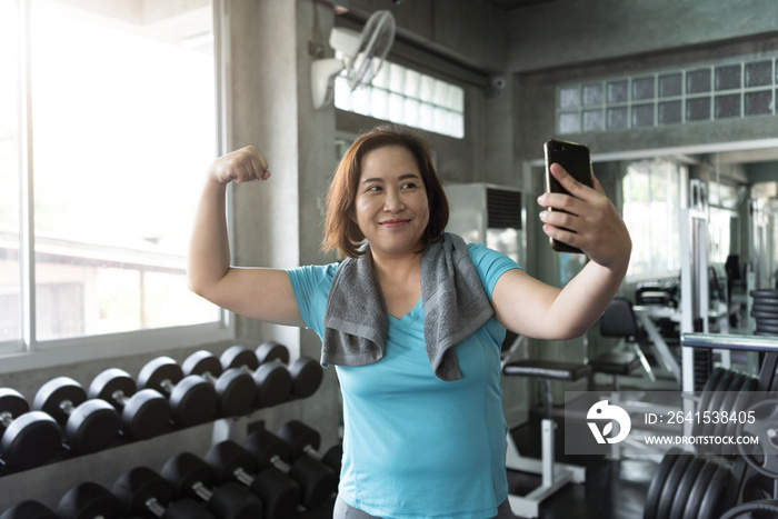 Senior asian woman attractive smiling active fitness in gym and taking a selfie showing muscle.