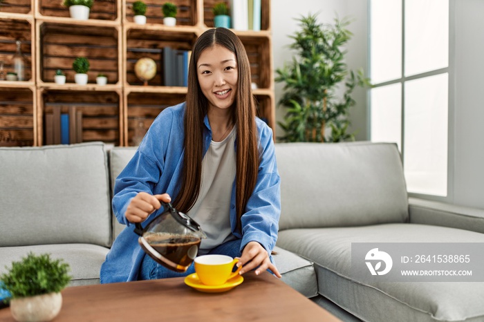 年轻的中国女孩坐在家里的沙发上喝咖啡。