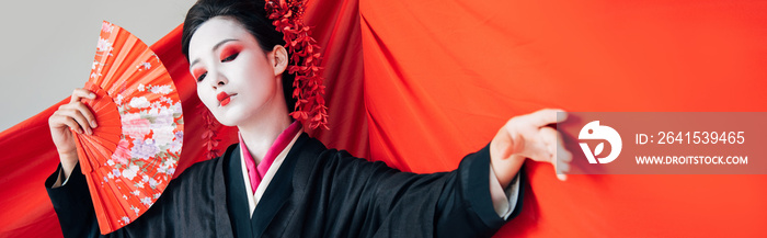 beautiful geisha in black kimono with hand fan and red cloth on background gesturing isolated on whi