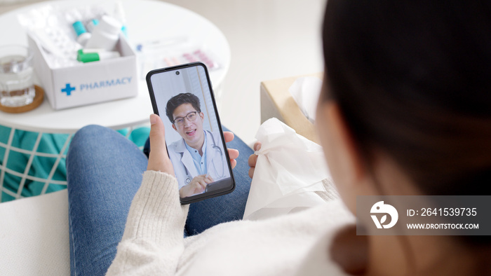 Over shoulder view of young asia woman talk to doctor on cellphone videocall conference medical app 