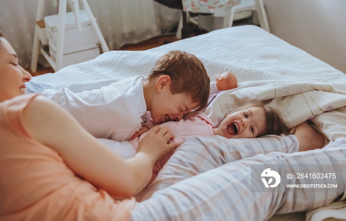 Relaxed mother and sons playing over the bed