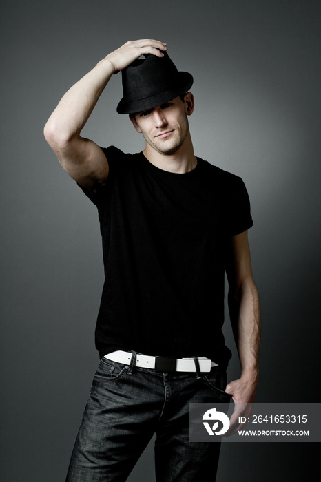 英俊的男子在黑色t恤和黑色帽子摆姿势。