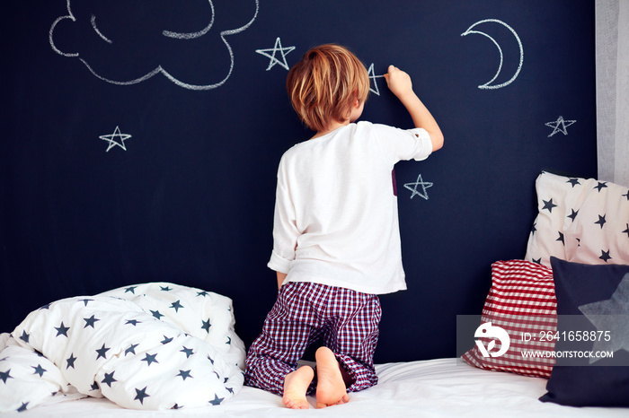 可爱的孩子穿着睡衣在卧室的黑板墙上画画