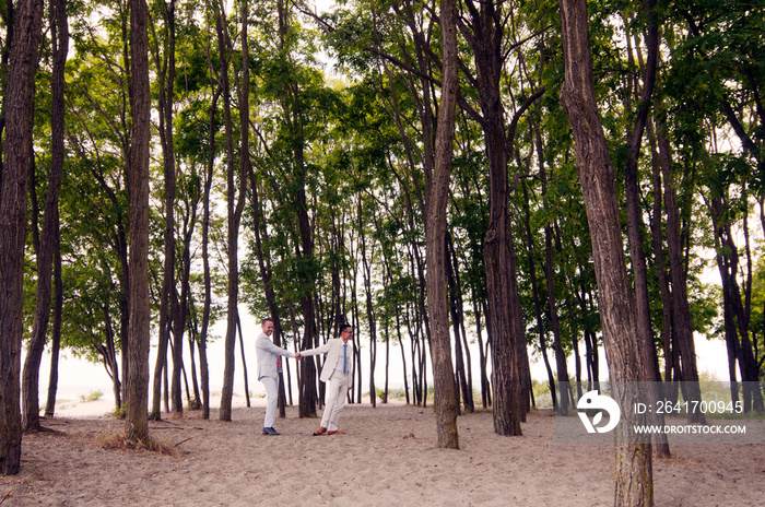 Happy gay couple holding hands while standing amidst trees at forest