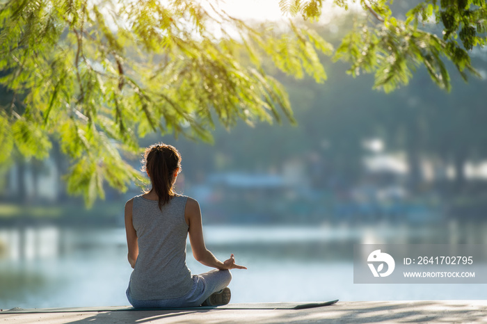 Beautiful woman practicing yoga waterfront in the park.